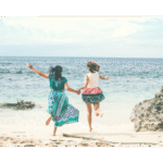 Two women holding hands and joyfully jumping on a sandy beach by the ocean, symbolizing vitality, connection, and freedom in midlife.