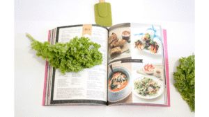 Open recipe book with healthy lunch ideas, fresh lettuce, and a green spatula on a white kitchen bench