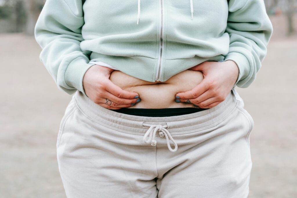 woman in a tracksuit holding her belly fat to signify menopasue weight gain